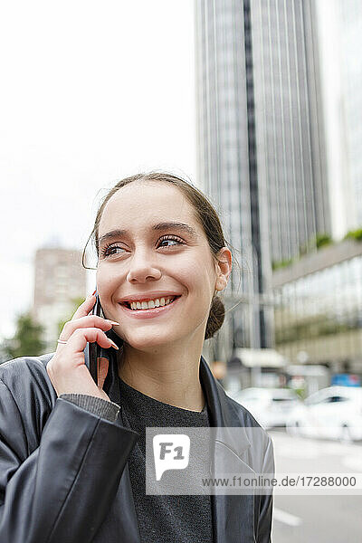 Lächelnde Unternehmerin  die wegschaut  während sie mit einem Mobiltelefon spricht
