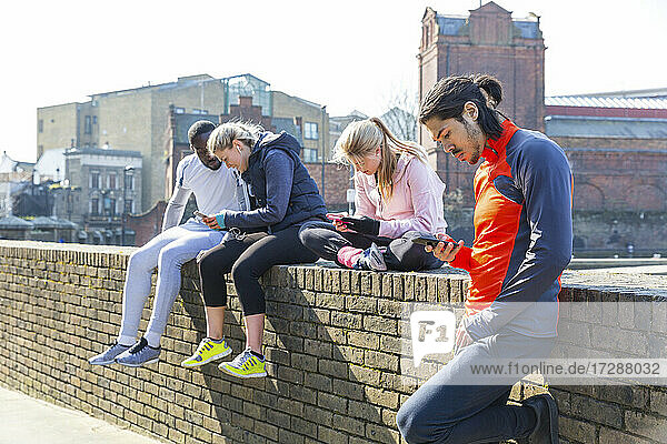 Multiethnische Fitnessfreunde nutzen Smartphones an der Wand