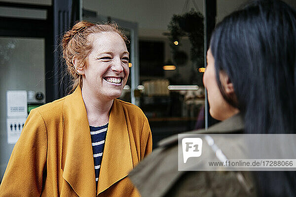 Happy woman looking at female friend outside cafe