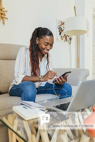 Smiling woman using mobile phone in living room at home
