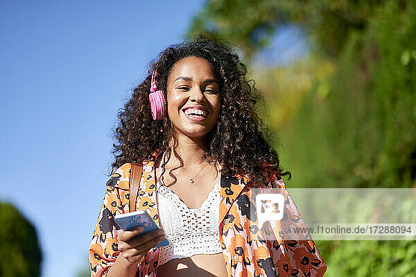 Smiling woman listening music through headphones on sunny day