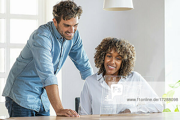 Geschäftsmann steht neben einem Kollegen  der ein futuristisches digitales Tablet im Büro benutzt