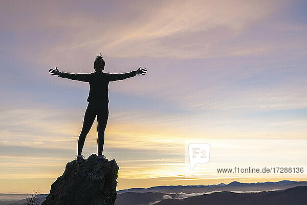 Young woman with arms outstretched standing on rock