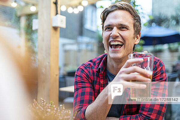 Mann lacht,  während er in einer Kneipe ein Bierglas hält