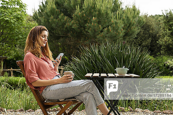Frau benutzt Smartphone  während sie auf einem Stuhl im Garten sitzt
