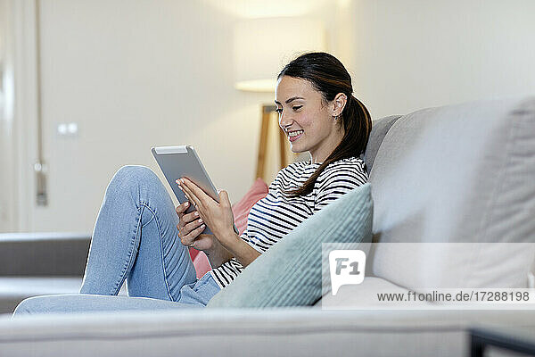 Lächelnde Frau mit digitalem Tablet auf dem Sofa im Wohnzimmer