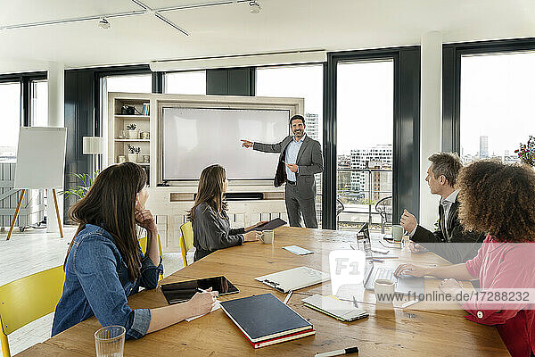 Smiling male professional explaining on projection screen to colleagues during meeting at office