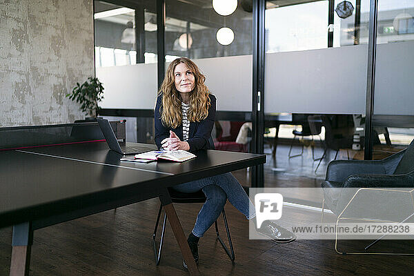 Businesswoman with hands clasped looking away while sitting at table in office