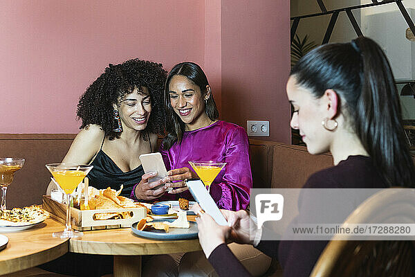 Freunde benutzen Mobiltelefone  während sie im Restaurant sitzen