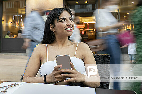 Junge Frau mit Mobiltelefon träumt in einem Straßencafé