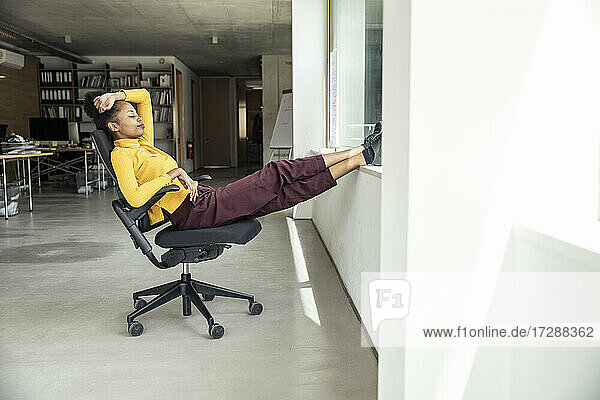 Geschäftsfrau mit hochgelegten Füßen entspannt auf einem Stuhl im Büro