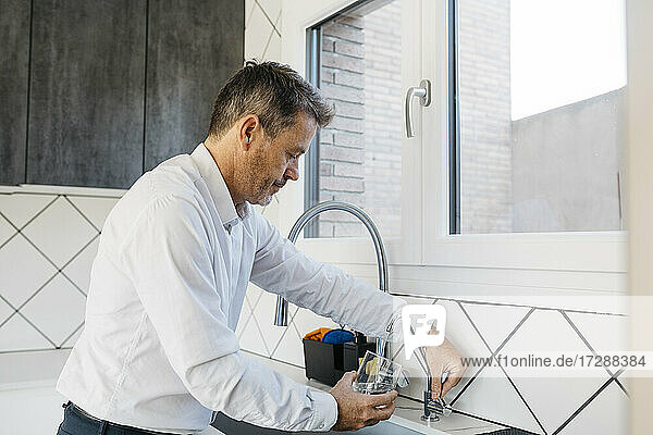 Geschäftsmann füllt Wasser durch den Wasserhahn in der Küche in ein Glas