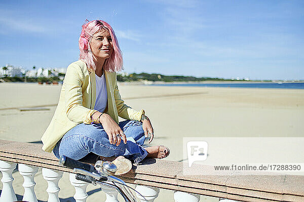 Lächelnde Frau auf der Promenade am Strand sitzend