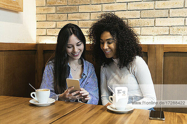 Freundinnen trinken Kaffee und benutzen dabei ihr Smartphone in einer Bar