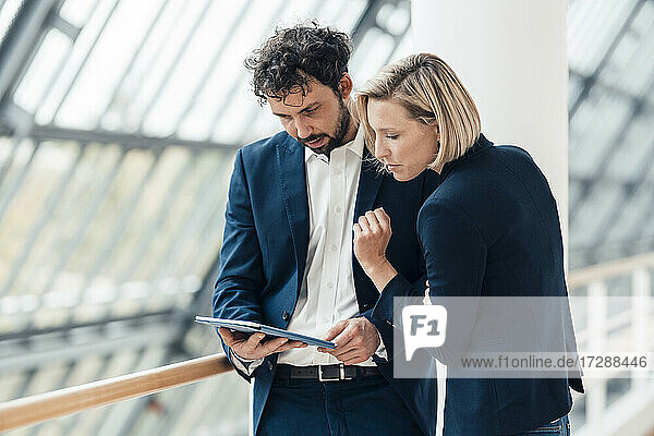 Businessman using digital tablet while standing by colleague in office