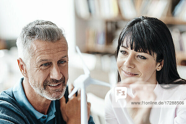 Lächelnde Geschäftsfrau  die mit einem Kollegen in einem Café das Modell einer Windkraftanlage überprüft