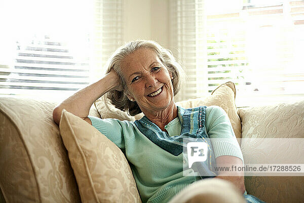 Lächelnde ältere Frau mit dem Kopf in der Hand auf dem Sofa zu Hause sitzend