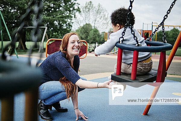 Mutter kitzelt ihren Sohn auf der Schaukel eines Spielplatzes im Park