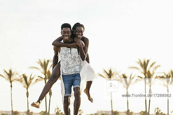 Happy man piggybacking teenage girl while running at beach