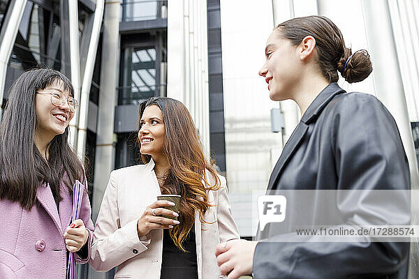 Unternehmerinnen mit Kaffeetasse und Aktenordner im Gespräch  während sie zusammen stehen