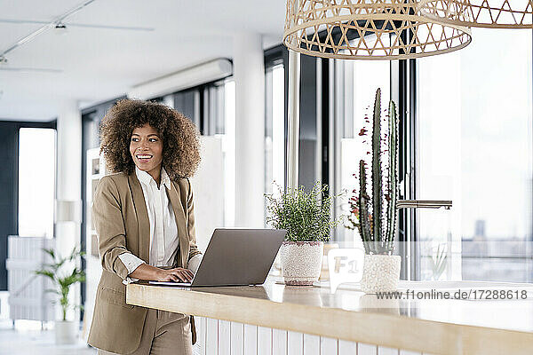 Afro-Geschäftsfrau lächelt  während sie mit einem Laptop an der Theke einer Büro-Cafeteria steht