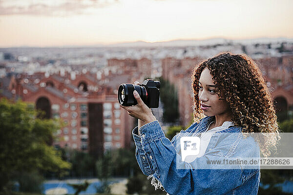Young woman photographing through camera by city