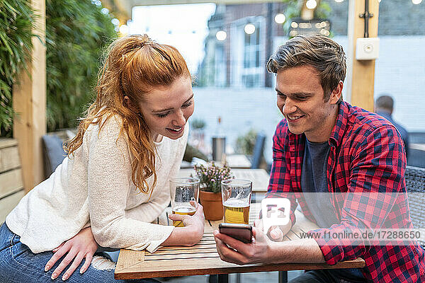 Couple looking at smart phone while having beer at pub