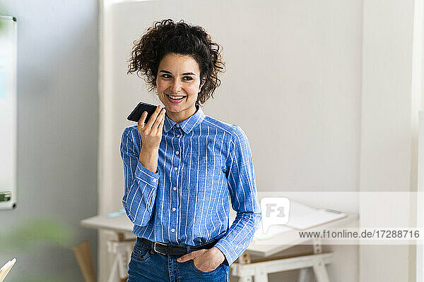 Smiling businesswoman with hand in pocket talking on mobile phone at office