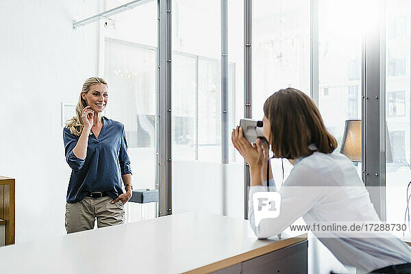Junge Unternehmerin fotografiert eine Mitarbeiterin mit einer Sofortbildkamera im Büro
