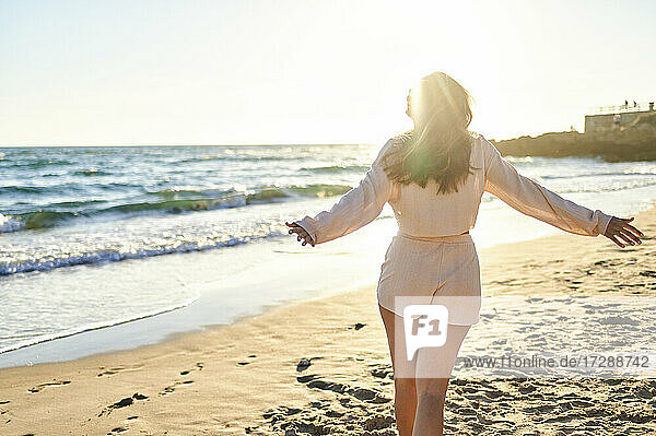 Woman with arms outstretched walking on shore at beach