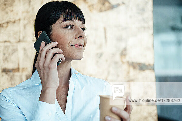 Unternehmerin hält Kaffeetasse und spricht mit dem Handy