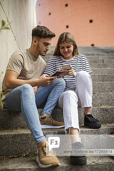 Paar benutzt Mobiltelefon  während es auf einer Treppe sitzt