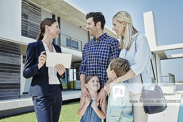 Businesswoman with digital tablet smiling while standing with family in front of villa