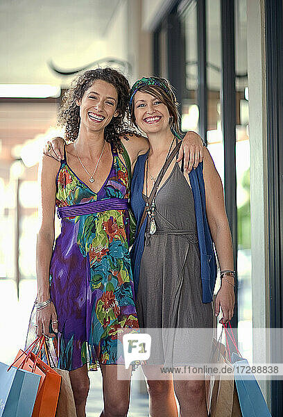 Smiling female friends carrying shopping bags while standing with hands on shoulders