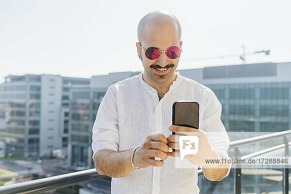 Lächelnder Mann  der ein Smartphone benutzt  während er auf einem Balkon steht