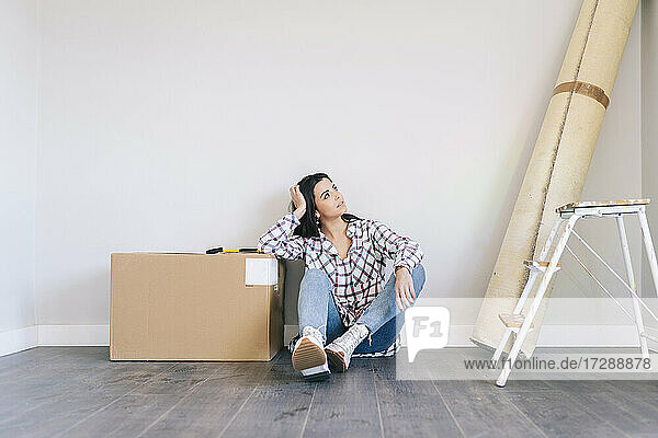 Nachdenkliche Frau sitzt bei einer Schachtel auf dem Boden zu Hause