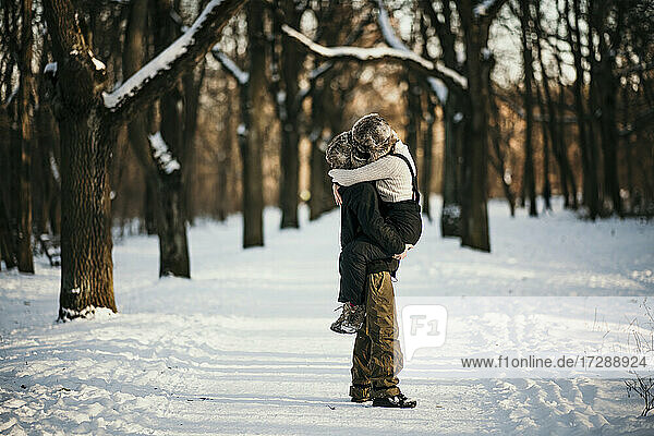 Freund trägt seine Freundin im Schnee stehend im Wald