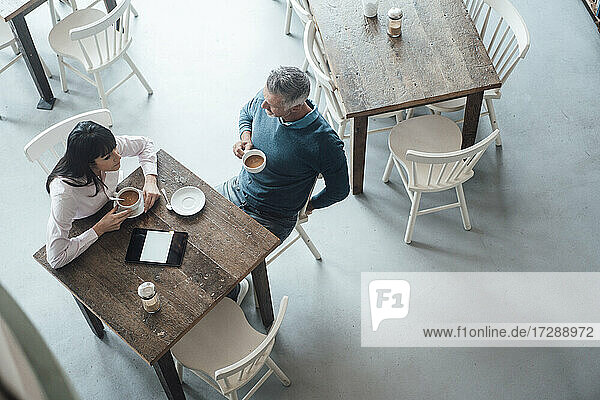 Männlicher Unternehmer hört einem Kollegen zu  während er in einem Café sitzt