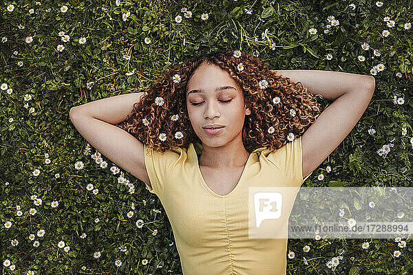 Young woman with hands behind head relaxing on meadow