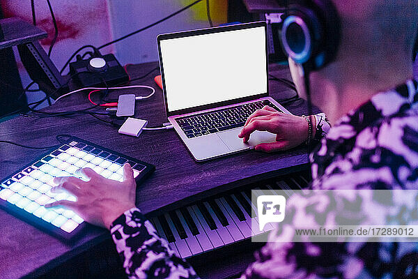 Männlicher Komponist mit Kopfhörern bei der Arbeit mit Laptop und digitalem Tablet im Studio