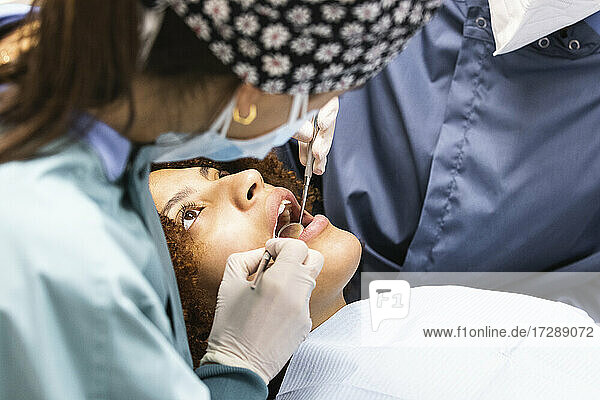 Female dentist checking patient's teeth with colleague in clinic during pandemic