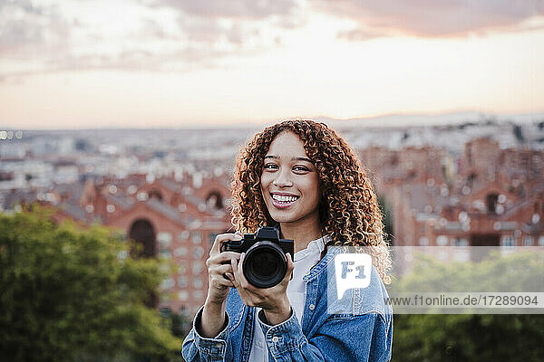 Lächelnde Frau hält Kamera bei Sonnenuntergang
