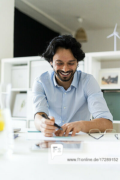 Lächelnder männlicher Unternehmer  der am Schreibtisch sitzt und arbeitet