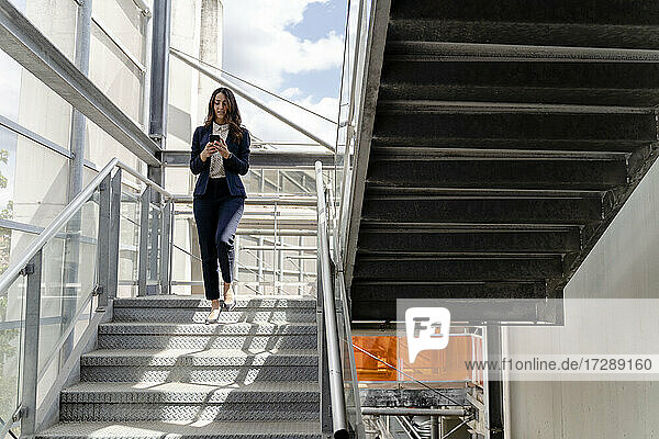 Geschäftsfrau  die ein Smartphone benutzt  während sie eine Treppe in einem Gebäude hinuntergeht