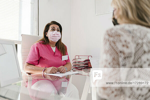 Female aesthetician in protective face mask discussing with woman at clinic