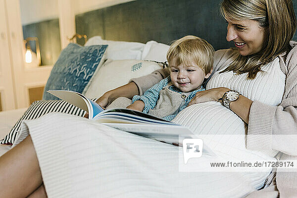 Niedlicher Junge schaut Fotoalbum mit schwangerer Mutter im Schlafzimmer an