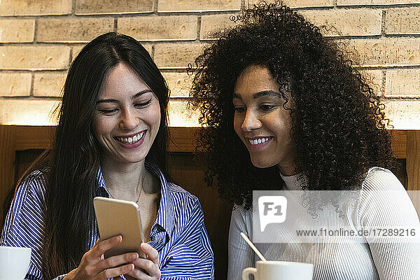 Lächelnde Freundinnen mit Smartphone in einer Bar