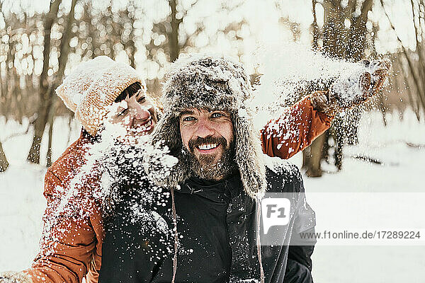 Lächelnde Freundin wirft Schnee auf Mann im Wald