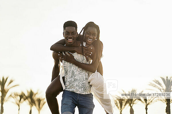 Cheerful man piggybacking girlfriend at beach