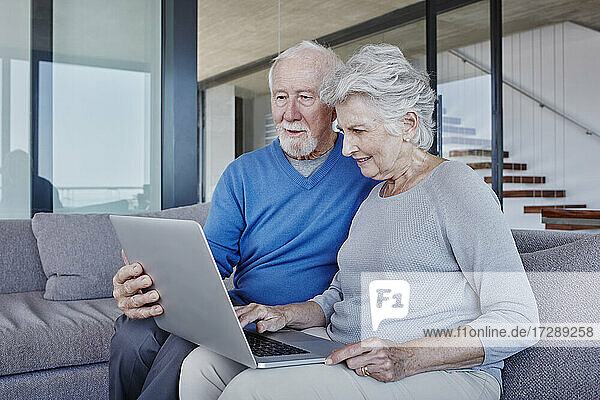 Senior couple using laptop sitting on sofa in living room